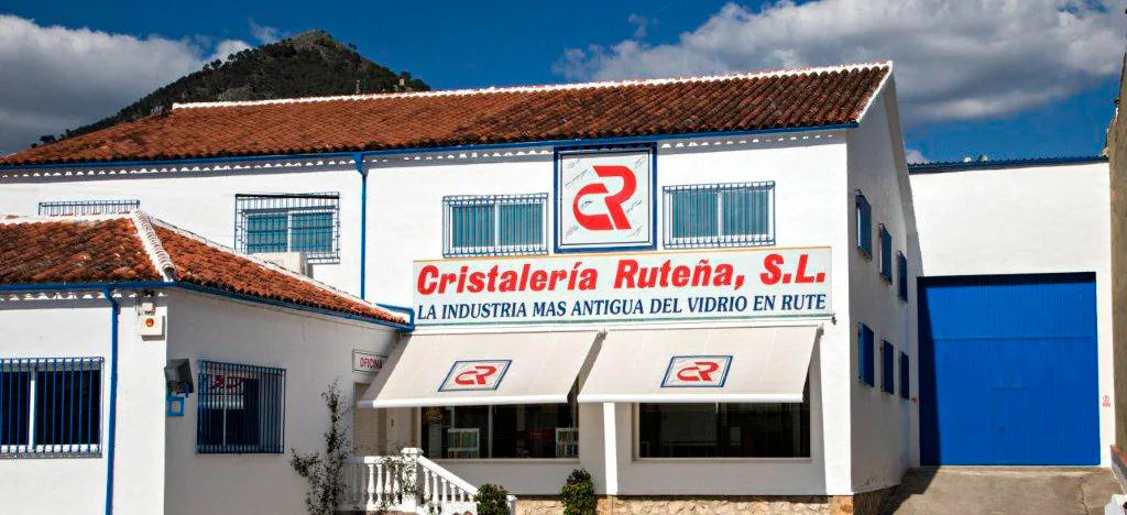 Fachada blanca del taller de Cristalería Ruteña en Rute, con el rótulo “Cristalería Ruteña, S.L. — La industria más antigua del vidrio en Rute” y el logotipo CR en rojo.